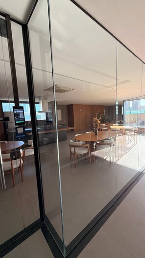 A modern interior with glass partitions, a dining area with round tables, and a visible digital screen. - New Listing (Maceió)