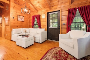 A cozy log cabin interior with a sectional sofa, a single armchair, and a wooden floor. - Bearly Behavin - Smart Cabin, Hot Tub & Fire Pit (Sevierville)