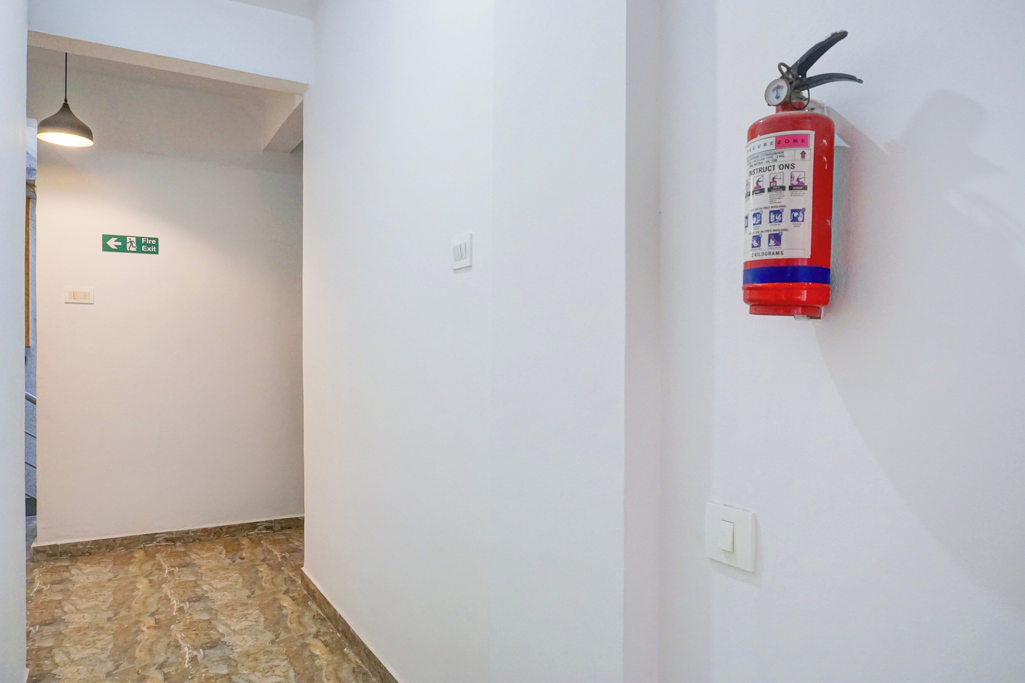 A hallway with a fire extinguisher mounted on the wall, a fire exit sign, and a light fixture.