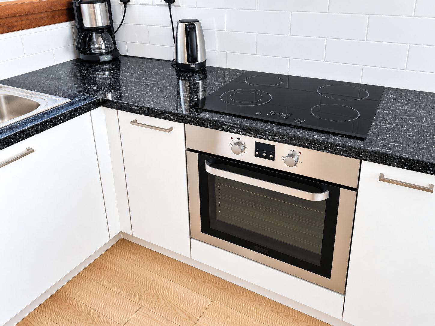 Cocina con armarios blancos, encimera negra y horno de acero inoxidable.