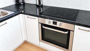Cocina con armarios blancos, encimera negra y horno de acero inoxidable.
