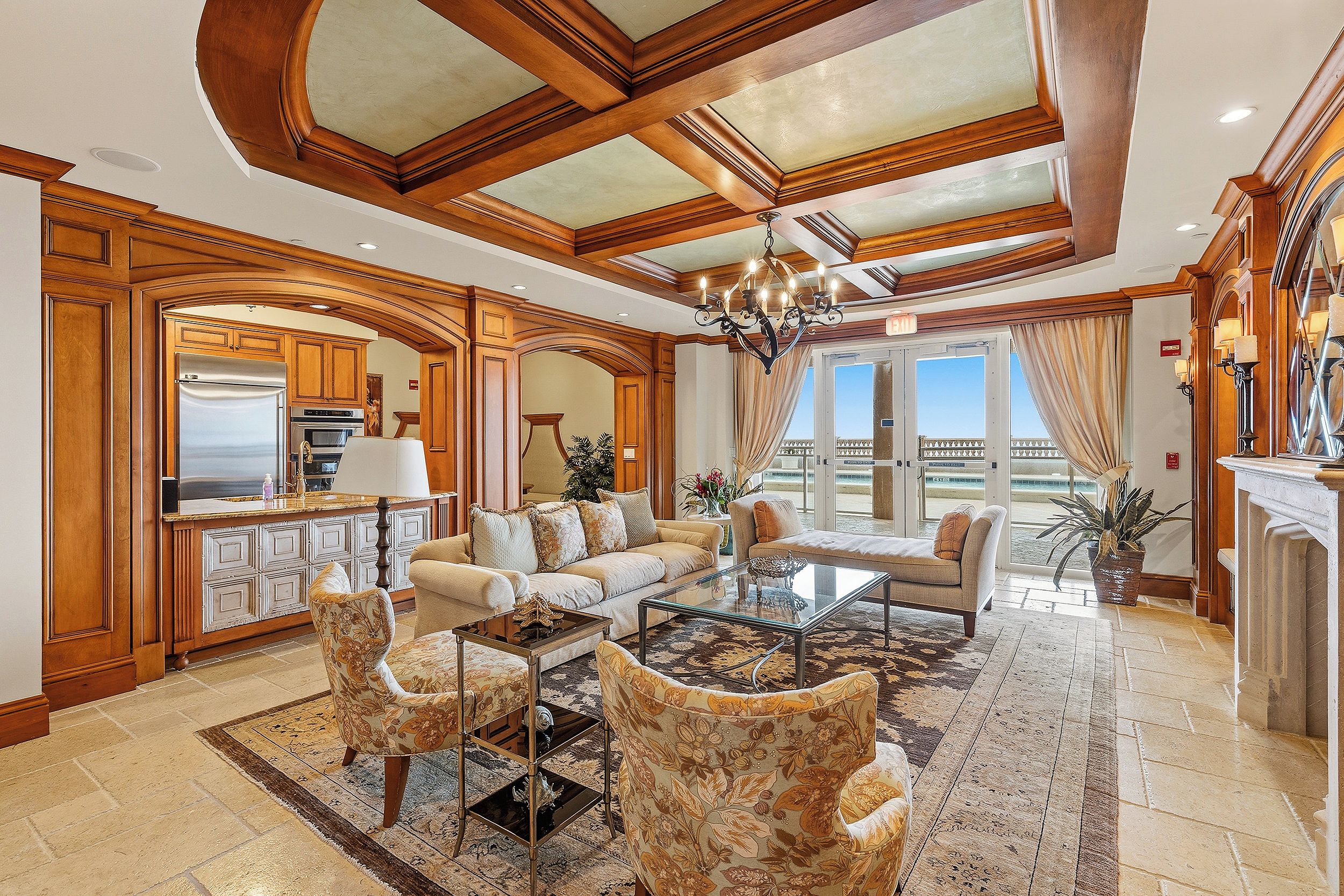 A spacious living room with a high ceiling, a chandelier, and a view of the outdoors.