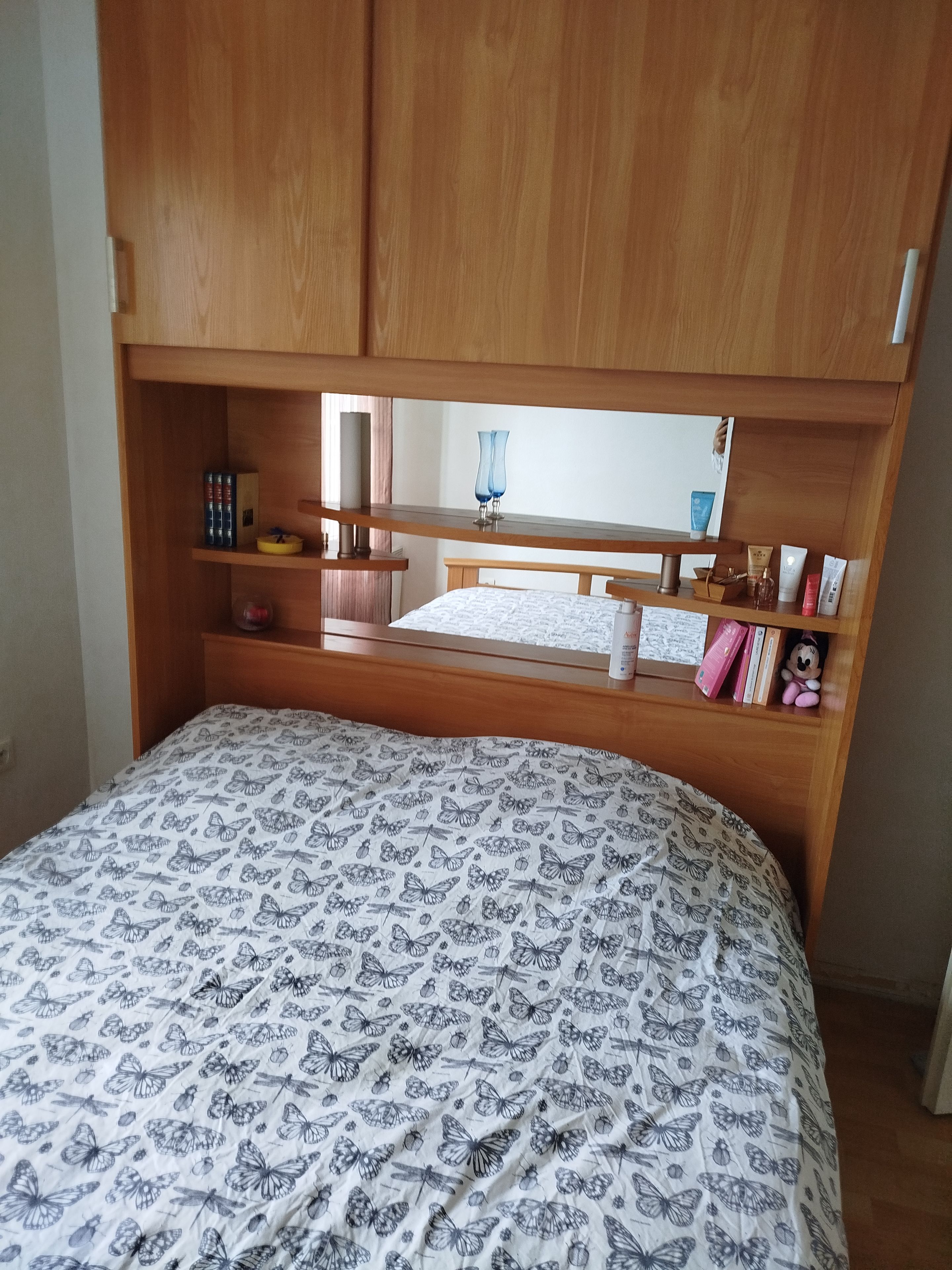 A bedroom with a bed, wooden headboard, shelves, and a mirror.