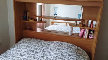 A bedroom with a bed, wooden headboard, shelves, and a mirror.
