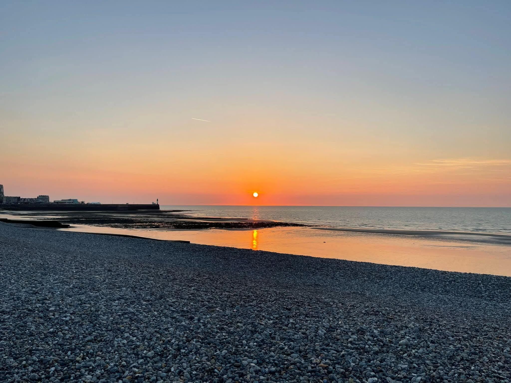 Ein Kiesstrand mit Sonnenuntergang über dem Wasser.