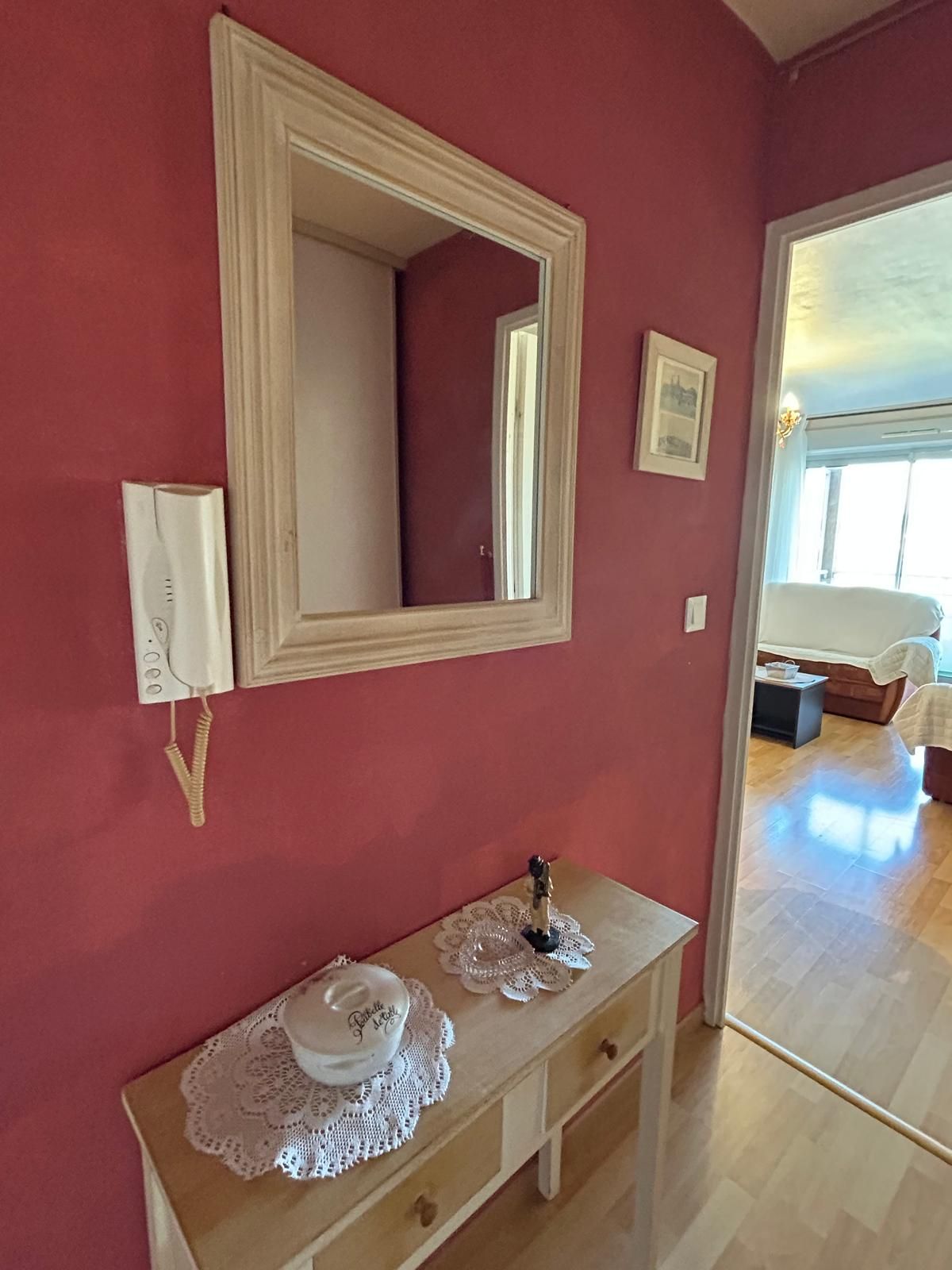 Une pièce dotée d’un grand miroir, d’une table de chevet avec une lampe et d’une porte donnant sur une autre pièce.