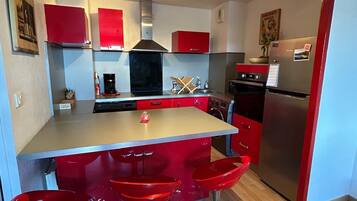 A modern kitchen with red cabinets, a central island with stools, stainless steel appliances, and a built-in oven.