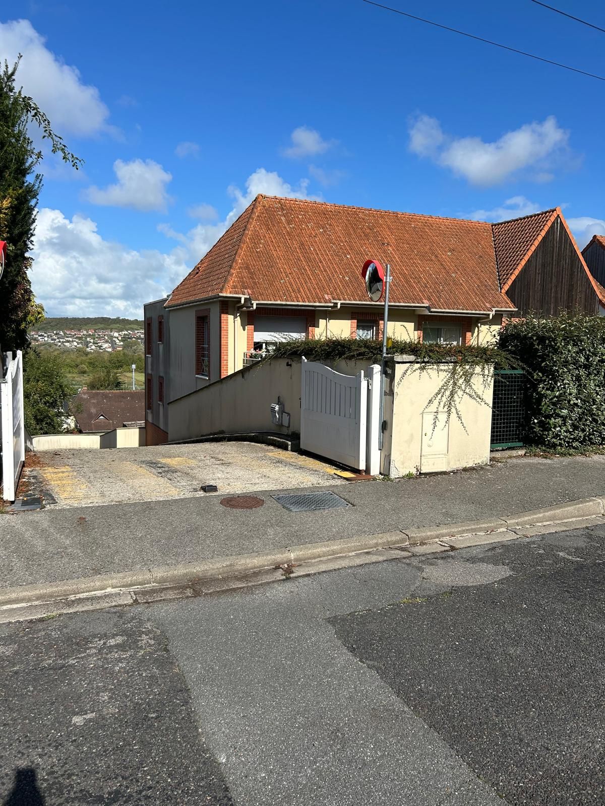 A residential building with a red-tiled roof, a gated driveway, and a clear sky.