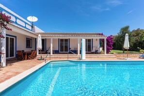 Ein Swimmingpool mit überdachtem Patio-Bereich, einem Esstisch mit Stühlen und einer Satellitenschüssel am Gebäude.