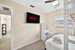 Een hotelkamer met een bed, bureau, stoel, een aan de muur bevestigde televisie en een raam met zonwering.