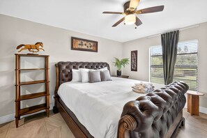 Ein Schlafzimmer mit einem großen Bett, einem Deckenventilator, einer Holzleiter und einem Fenster mit Jalousien.