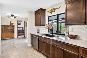 A kitchen with wooden cabinets, a stainless steel dishwasher, and a window with a view of the outdoors. - Oak Haven Retreat - Pool, Hot Tub & Fire Pit (Brandon)