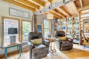 A cozy room with wooden beams, leather armchairs, a bookshelf, and a guitar.