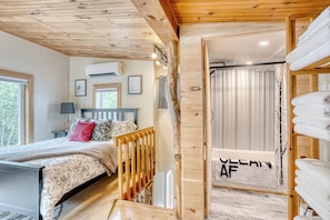 Une chambre à coucher comprenant un lit, une tête de lit en bois, une fenêtre, un appareil de climatisation et un porte-serviettes.