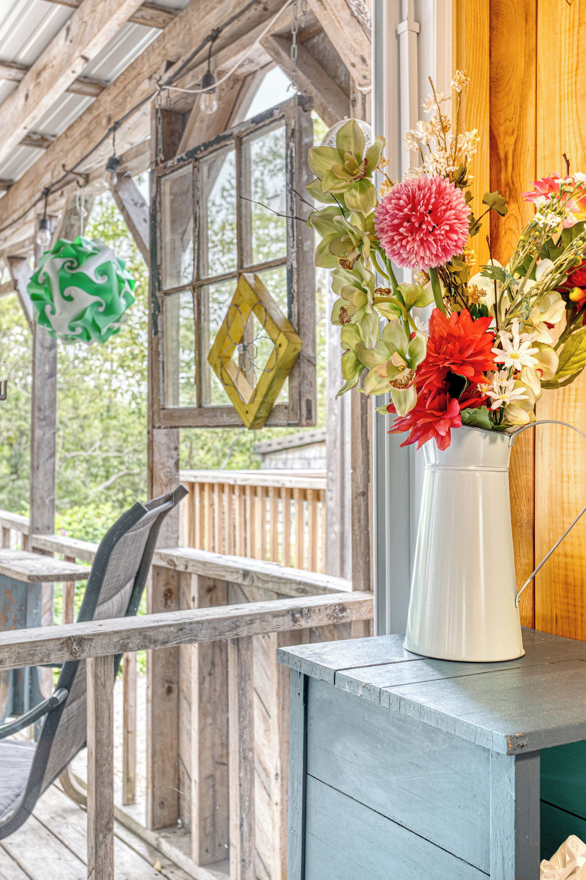 Une véranda en bois rustique, avec un vase blanc rempli de fleurs posé sur une table bleue.