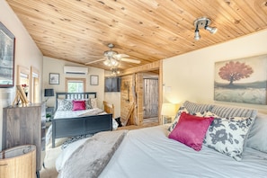 Une chambre avec un plafond en bois, un lit avec une literie à motifs, un tableau au mur et une fenêtre avec des rideaux.