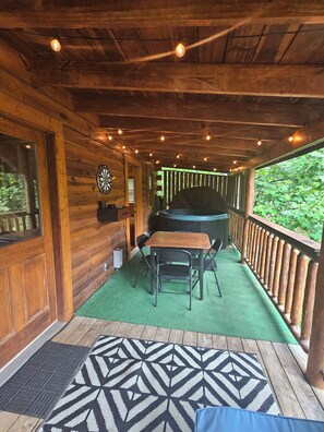 Eine Holzterrasse mit Tisch, Stühlen, einem Dartspiel und einem Whirlpool.
