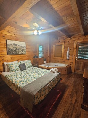 Ein Schlafzimmer einer Holzhütte mit Bett, Fenster mit Jalousien, einer Badewanne und einem Deckenventilator.