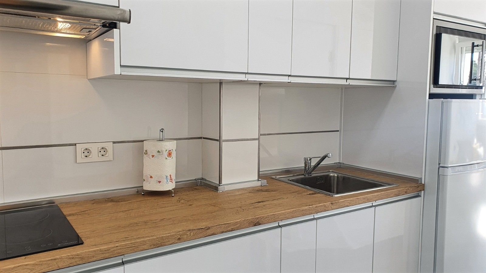 Een moderne keuken met witte kastjes, een houten aanrechtblad, een roestvrijstalen spoelbak en een inbouwoven.