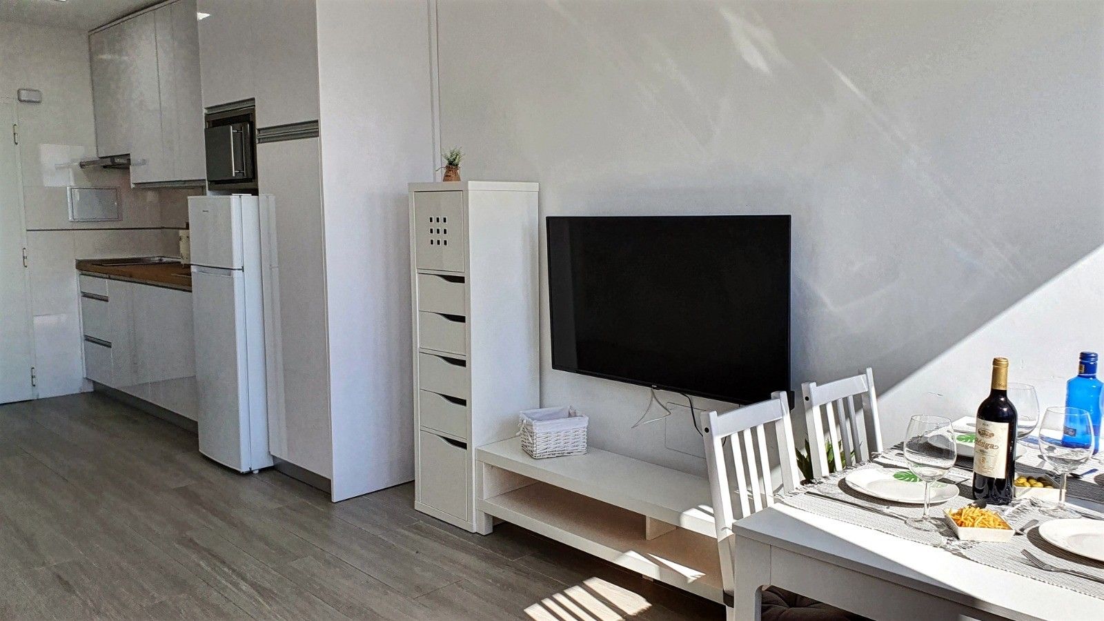 Una cocina moderna con armarios blancos, microondas integrado y televisor de pantalla plana.