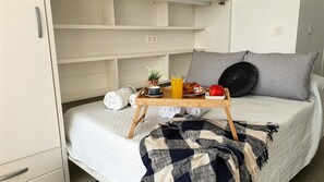 Una cama con una bandeja de alimentos para el desayuno, una almohada y una manta.
