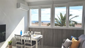 Un comedor con una mesa dispuesta para dos, un televisor en la pared y vistas al mar a través de amplios ventanales.