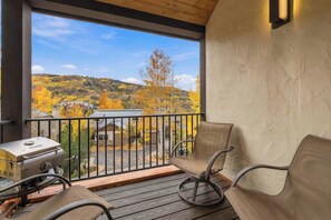 Un balcón con una parrilla, sillas y vistas a follaje otoñal y casas.