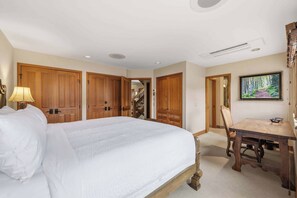 Habitación de hotel con una cama grande, un escritorio y una silla. Hay puertas de madera y un cuadro en la pared.