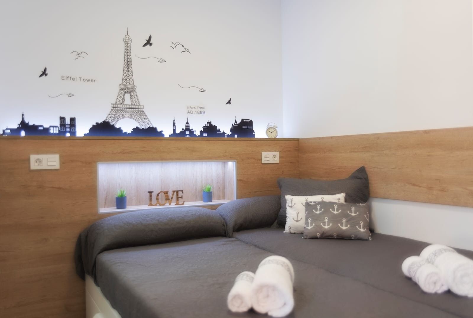 Una habitación de hotel con cama, almohadas, una decoración en la pared de la Torre Eiffel y un letrero con la palabra 'LOVE'.