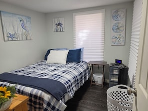 A bedroom with a bed, a bedside table with a digital clock, a window with blinds, and wall art. - Fabulous 1-bedroom studio in charming Norwich perfect for your stay. (Norwich)