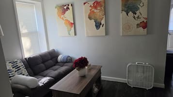 A living room with a grey sofa, a wooden coffee table with a vase, and three world maps on the wall.