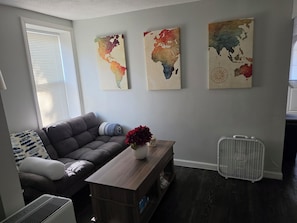 A living room with a grey sofa, a wooden coffee table with a vase, and three world maps on the wall. - Fabulous 1-bedroom studio in charming Norwich perfect for your stay. (Norwich)