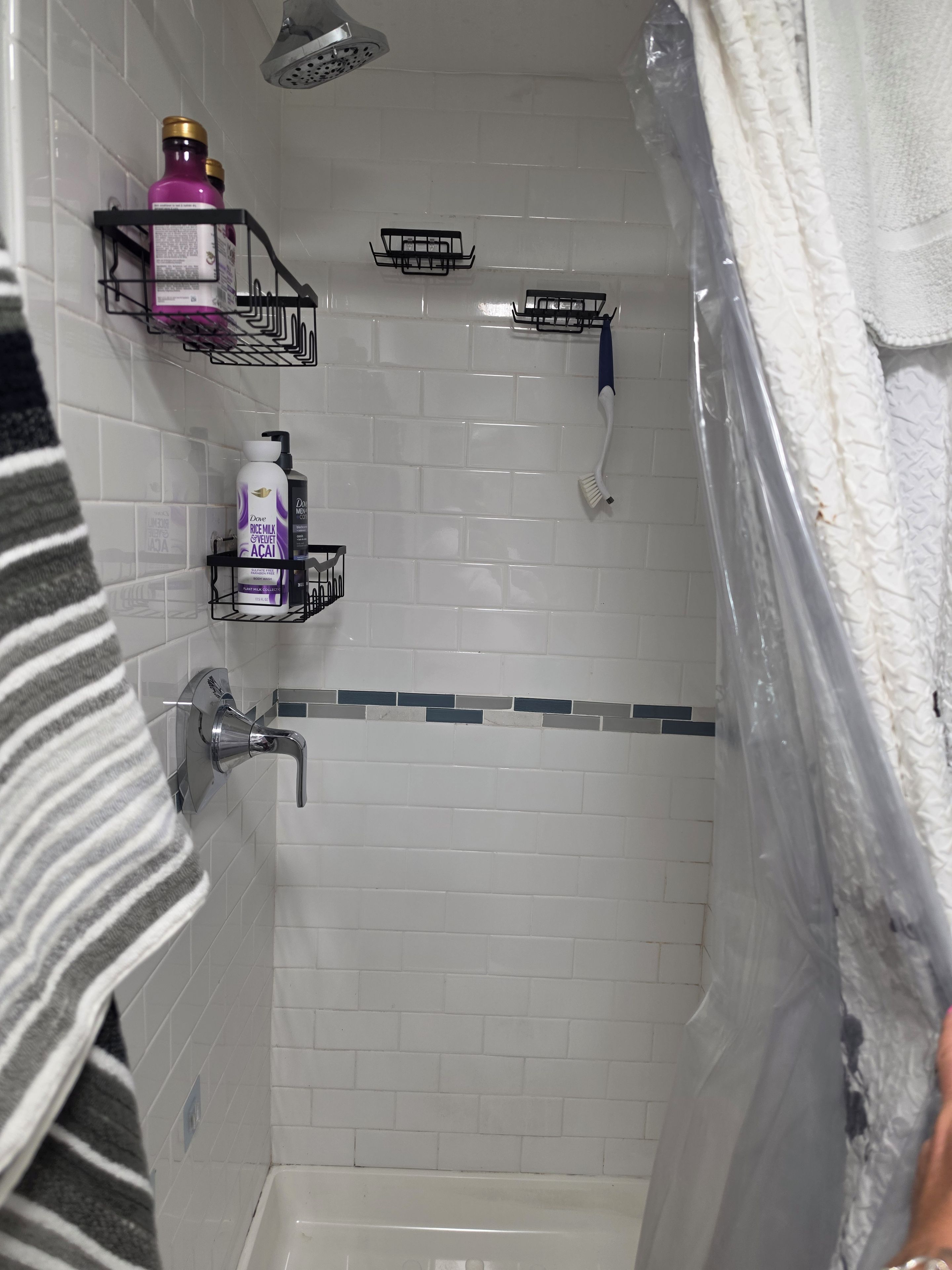 Une salle de bain avec des murs carrelés de carreaux blancs, une douche, des toilettes et un porte-serviettes.