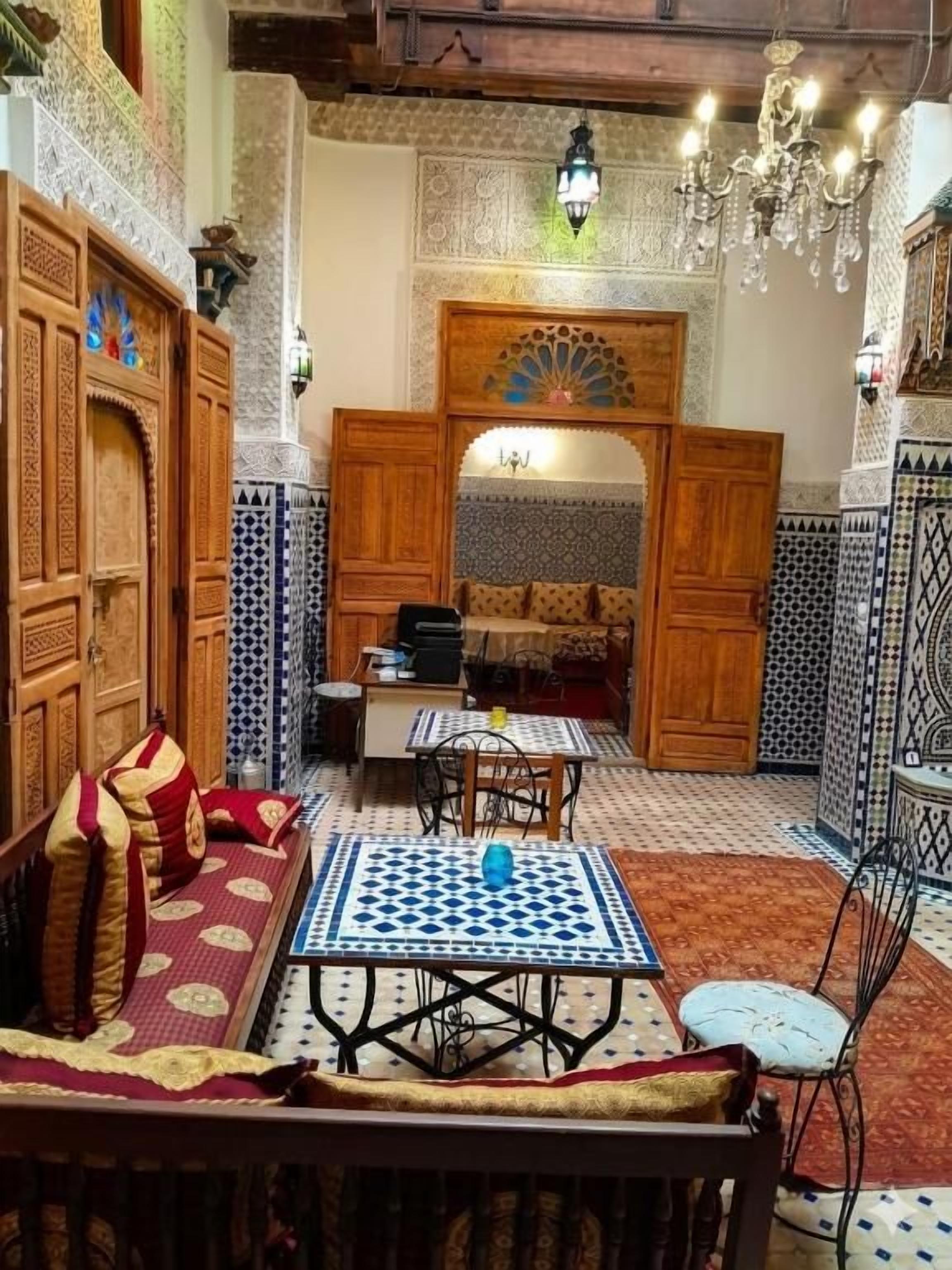Un interior tradicional marroquí con un sofá, una mesa con mantel blanco y azul estampado, y una araña.