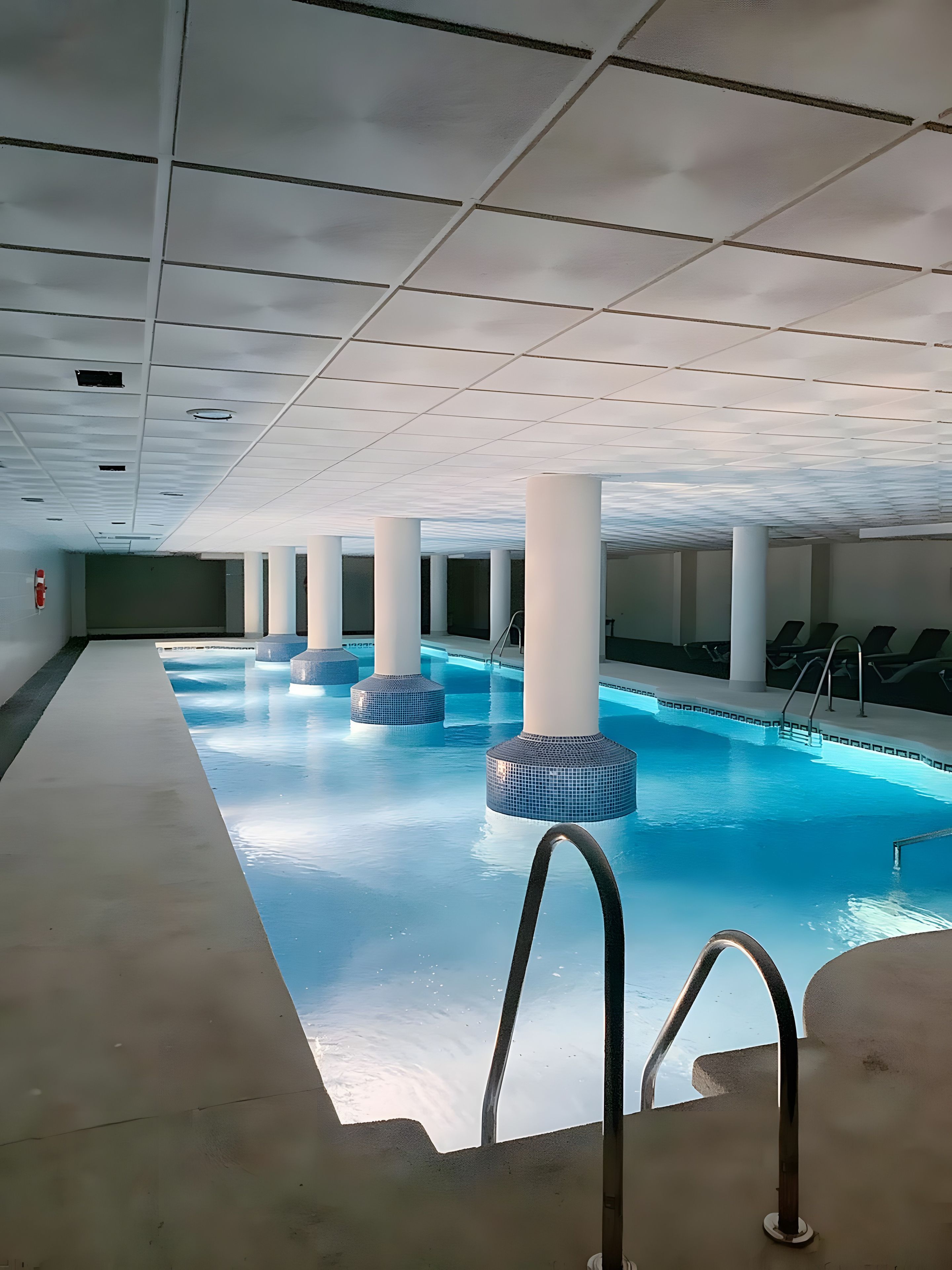 Una piscina interior con agua cristalina, rodeada de columnas blancas y un techo azulejado.