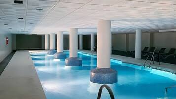 Una piscina interior con agua cristalina, rodeada de columnas blancas y un techo azulejado.