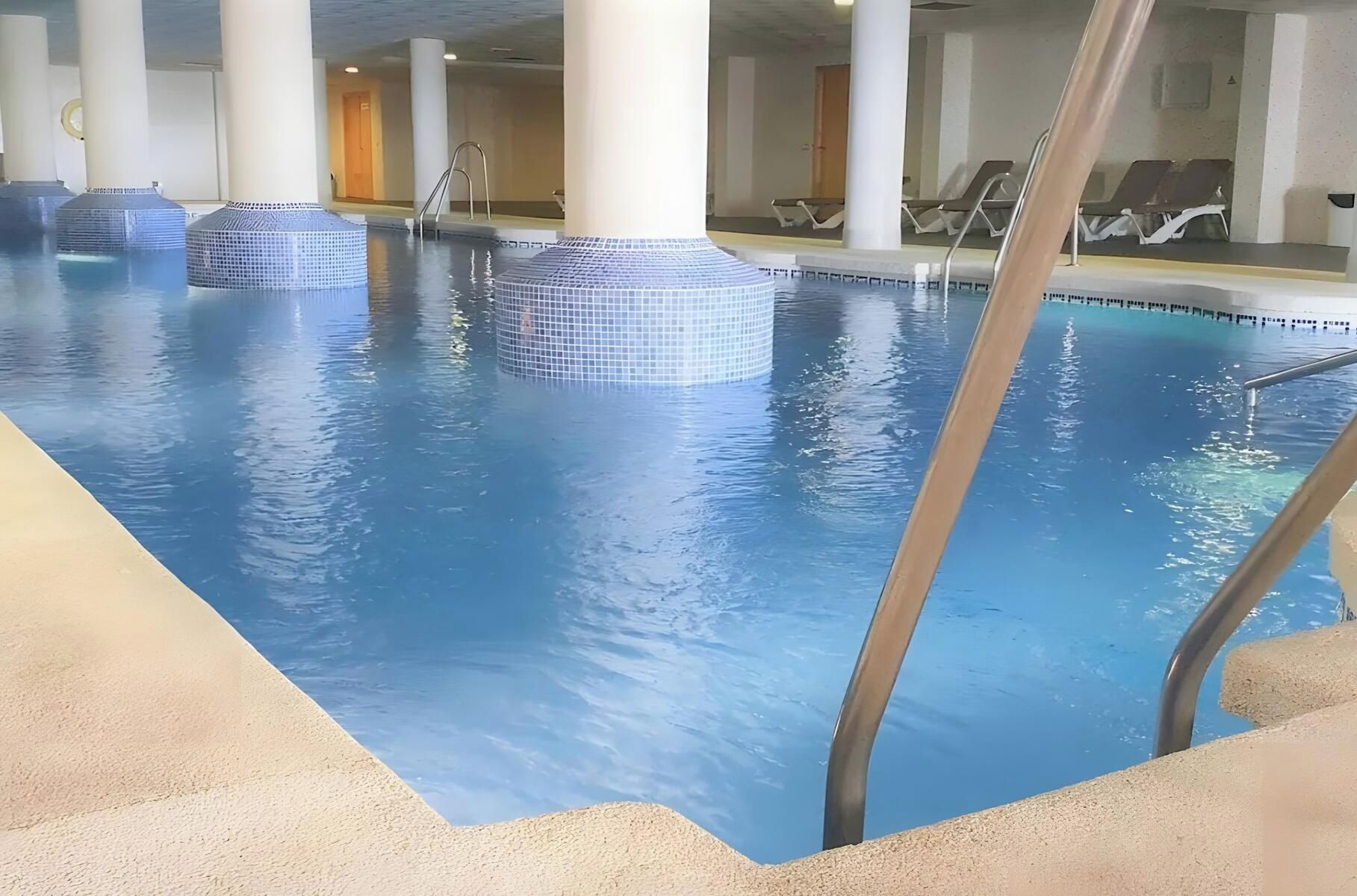 An indoor swimming pool with clear water, surrounded by columns and lounge chairs.