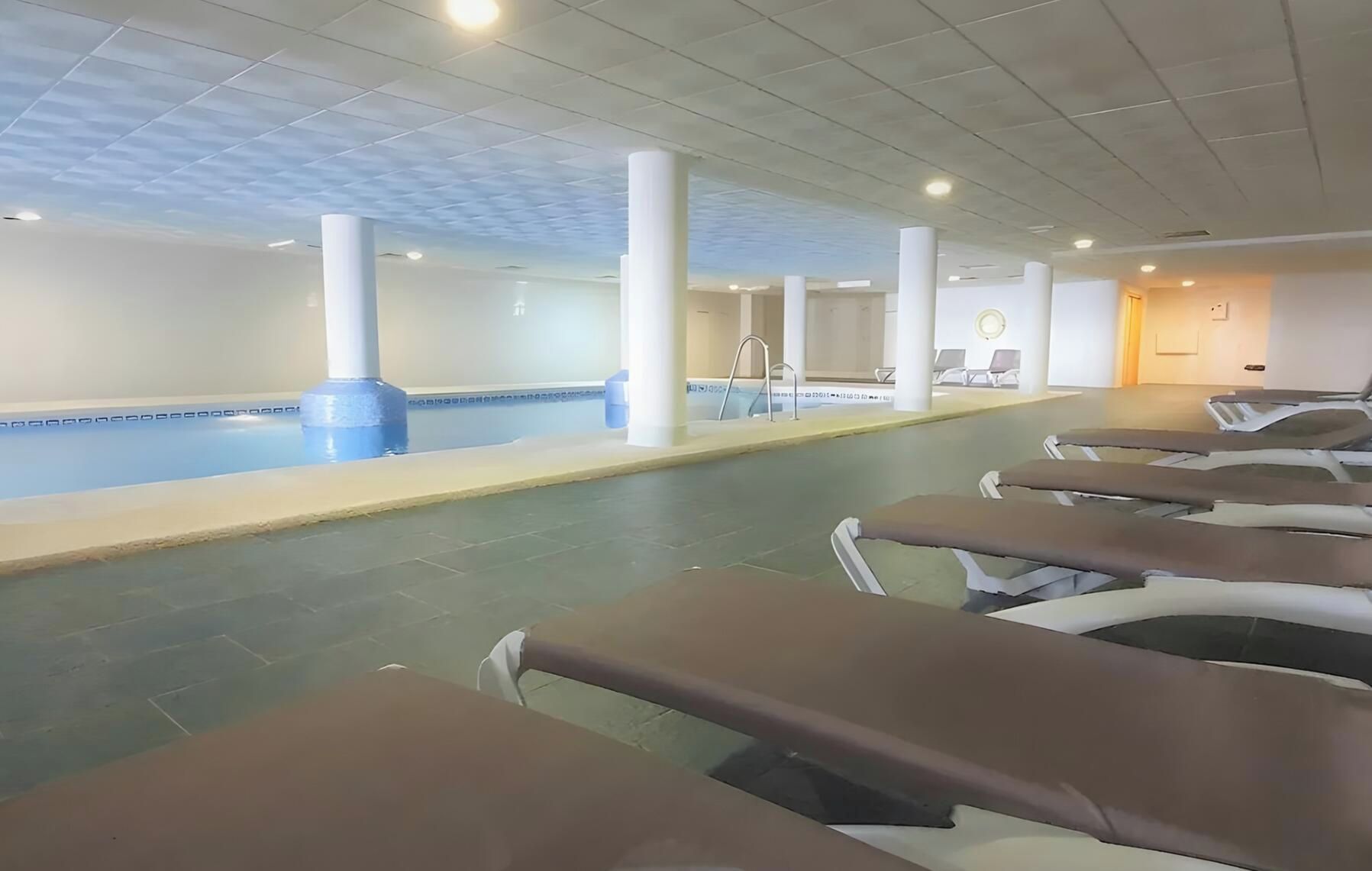A swimming pool area with lounge chairs and a ceiling with recessed lighting.