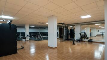 Een ruime fitnessruimte met diverse fitnessapparaten, een spiegelwand en een houten vloer.
