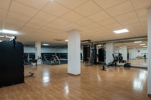 A spacious gym with various exercise equipment, a mirrored wall, and a wooden floor.