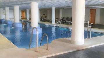Una piscina interior con agua cristalina, rodeada de columnas blancas, y equipada con escaleras metálicas para entrar y salir.