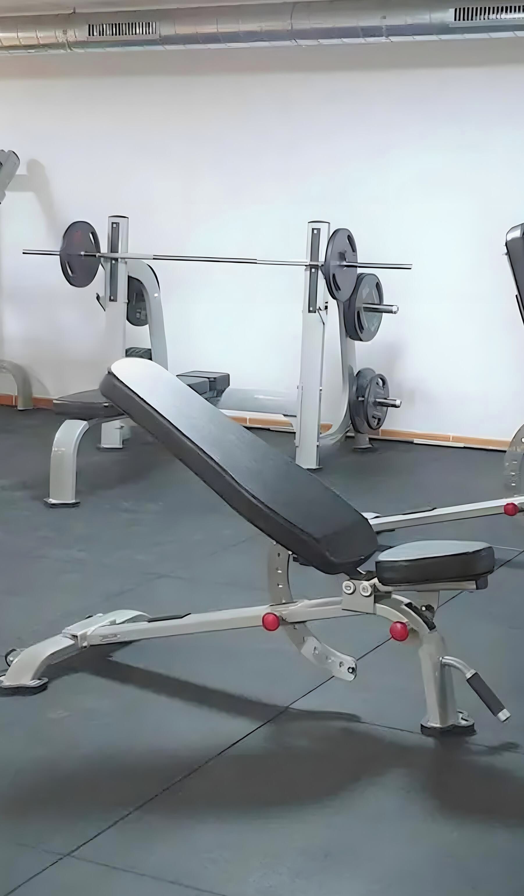 Un gimnasio con equipo de ejercicio, incluyendo una banca y máquinas de pesas.