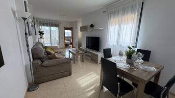 Una sala de estar moderna con sofá, televisor, comedor y zona de cocina.
