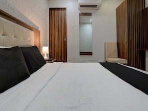 Habitació d'hotel amb un llit, una tauleta de nit amb una làmpada, una cadira, un armari i un aparell d'aire condicionat.