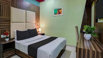 A hotel room with a bed, bedside table, lamp, and a potted plant.