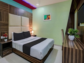Habitació d'hotel amb un llit, una taula de nit, una làmpada i una planta en test.