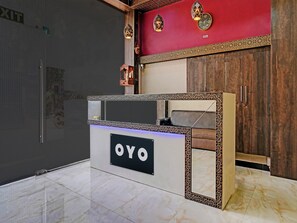 A reception desk with a sign reading 'OYO' in a modern lobby with a red accent wall and patterned tile border. - Classic Hotel Blue Sapphire (Mumbai)
