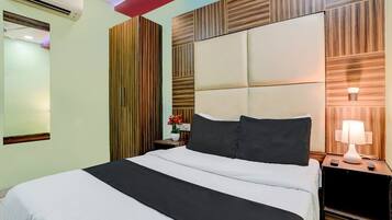 A hotel room with a bed, bedside table, lamp, and an air conditioning unit.