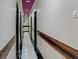 A corridor with a marble floor, white walls, and a wooden baseboard. - Classic Hotel Blue Sapphire (Mumbai)