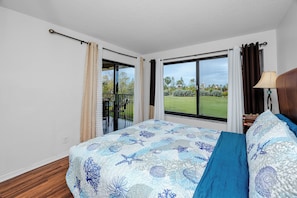 A hotel room with a bed, a window with a view of a golf course, and a balcony with a chair. - Relaxed Island Living Condo Golf Course Views (St.Petersburg)